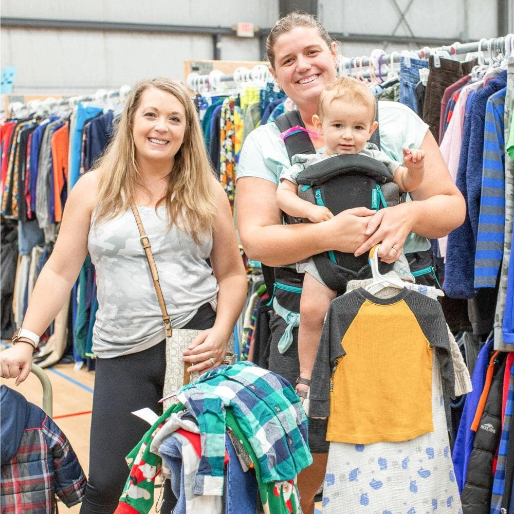 Two friend and baby in a carrier shopping together for baby clothing