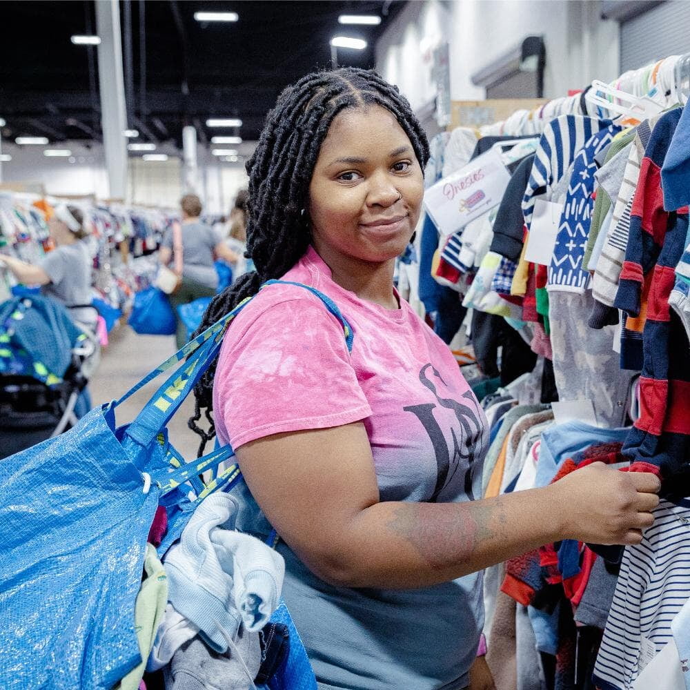 A mother stands next to clothing as she shops her local JBF sale.