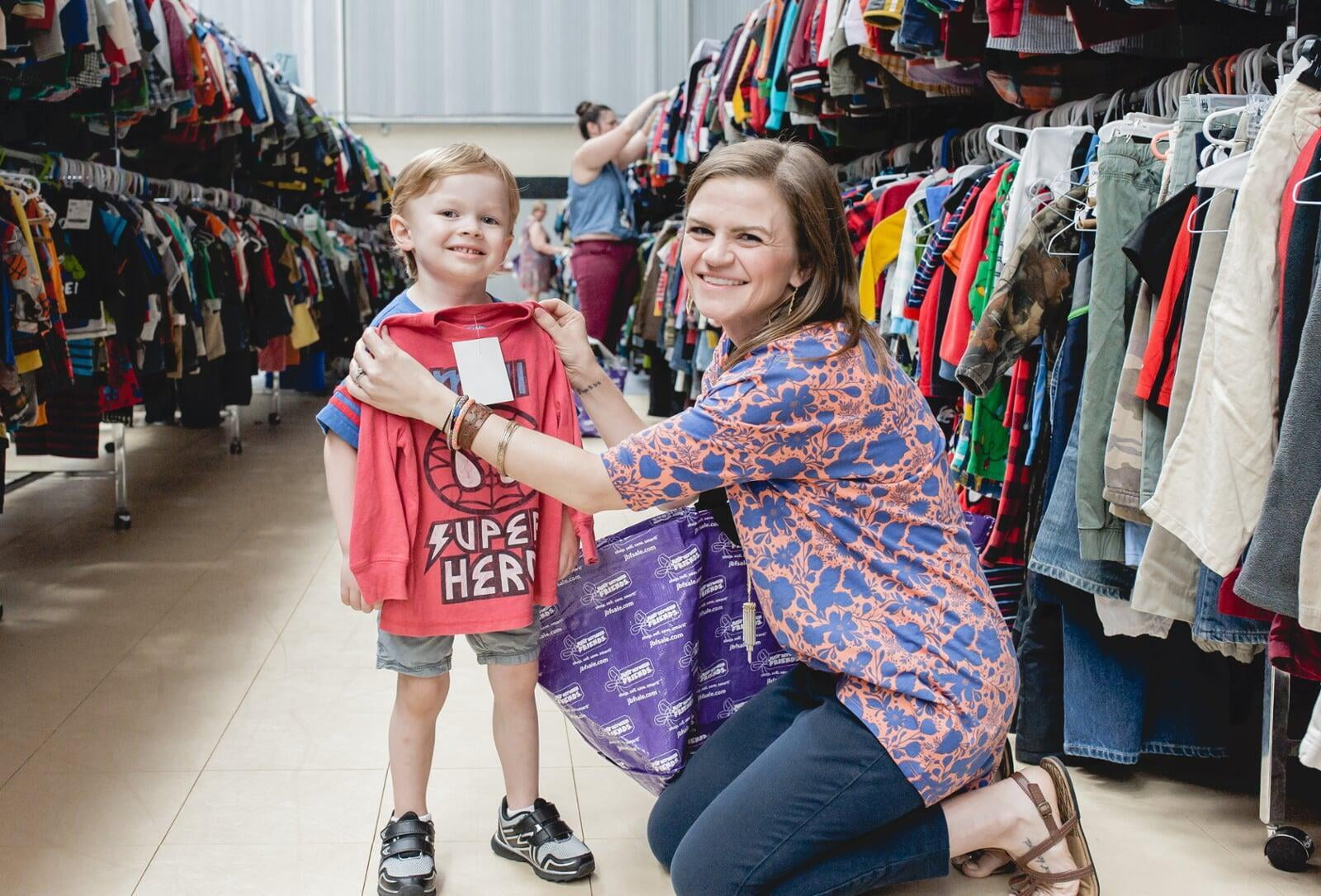 A mom and her four-year-old son stand with their masks and shopping bag in front of baskets of books and costumes.